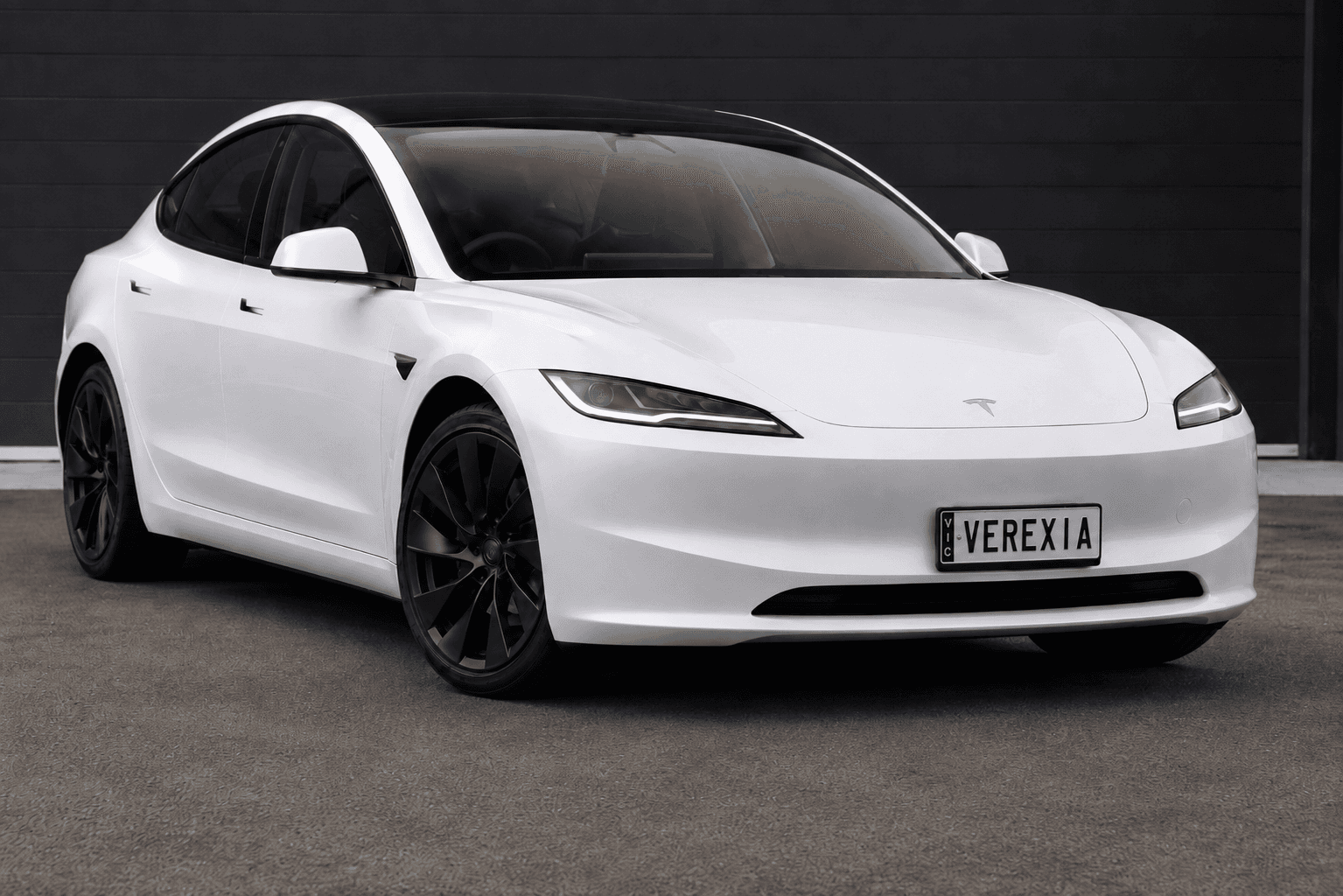 White Tesla Model 3 with a Verexia number plate, against a dark wall